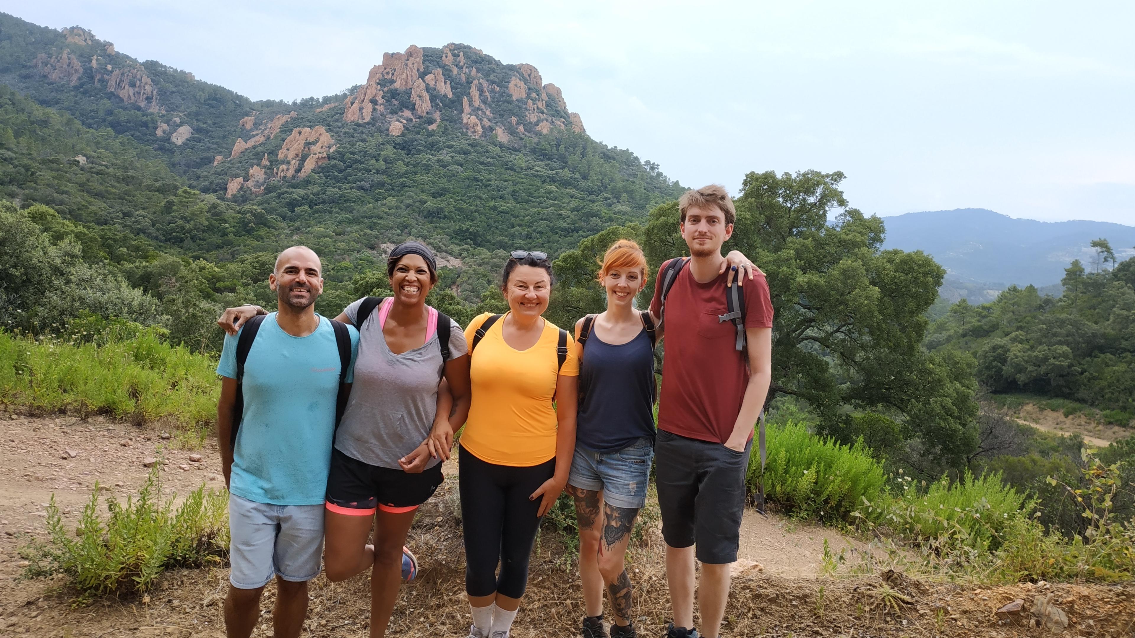 Five smiling people with rocky hills and Mediterranean vegetation behind them